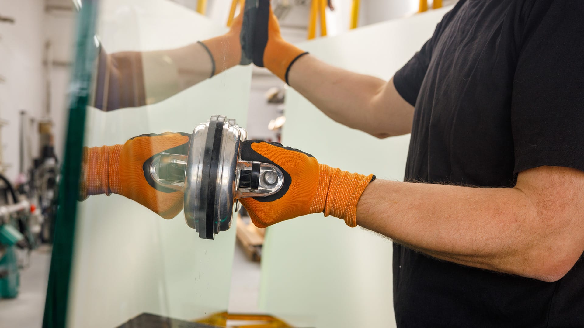 Profissional com luvas de segurança manuseando uma chapa de vidro espessa com uma ventosa de sucção em uma fábrica ou vidraçaria.
