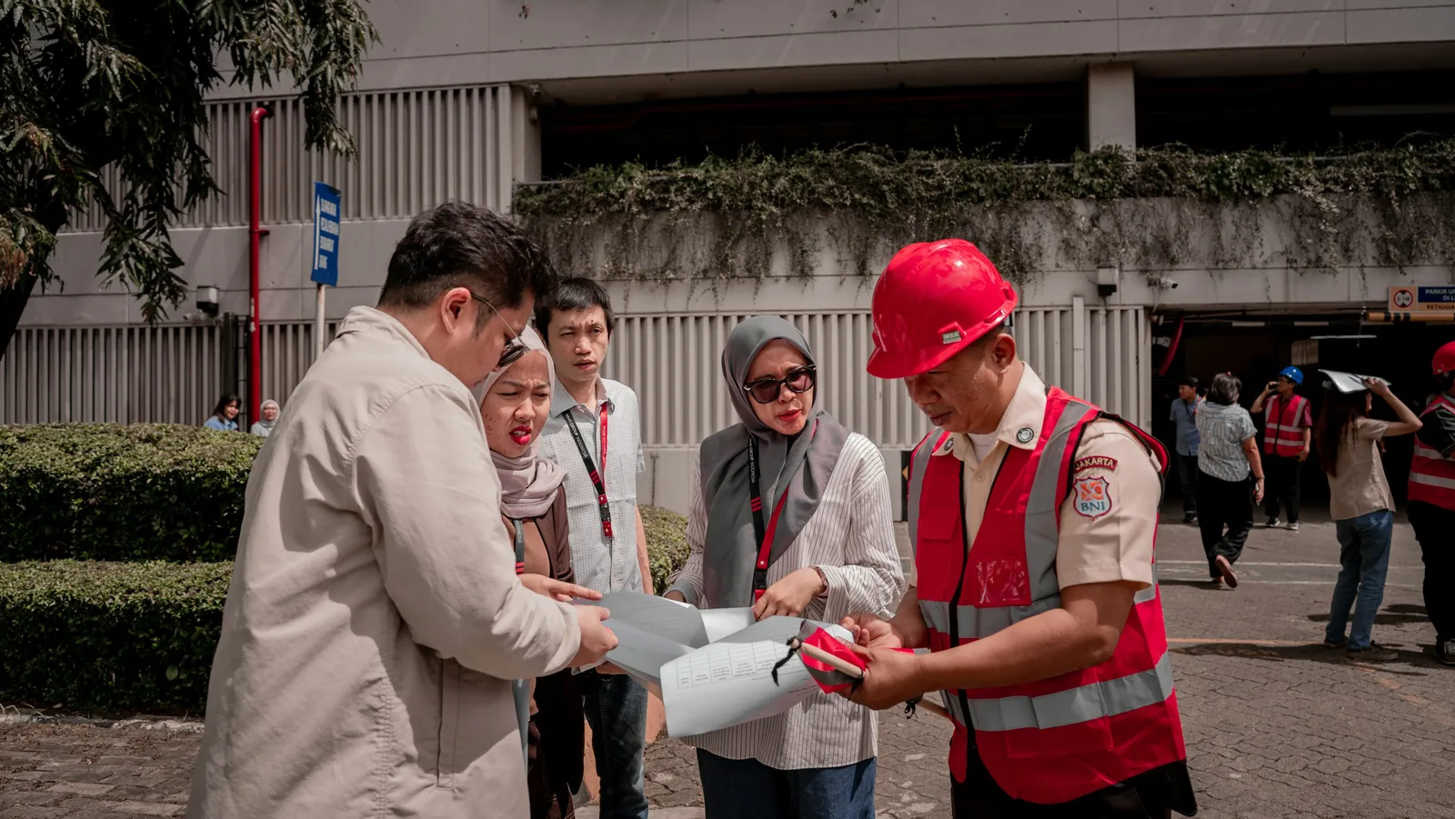 Grupo de profissionais analisa planta técnica durante vistoria em obra, com responsável técnico de capacete vermelho ao centro