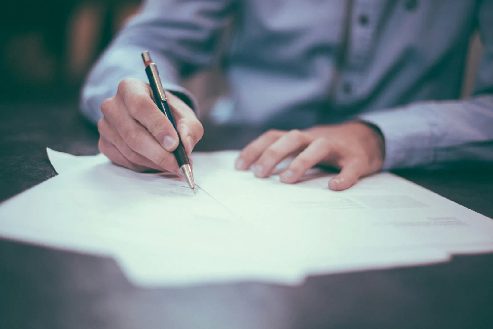 Mão assinando contrato de prestação de serviço de manutenção predial sobre mesa de escritório