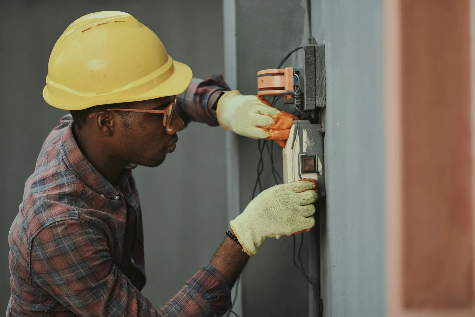Técnico com capacete instalando fiação em quadro elétrico durante manutenção predial preventiva