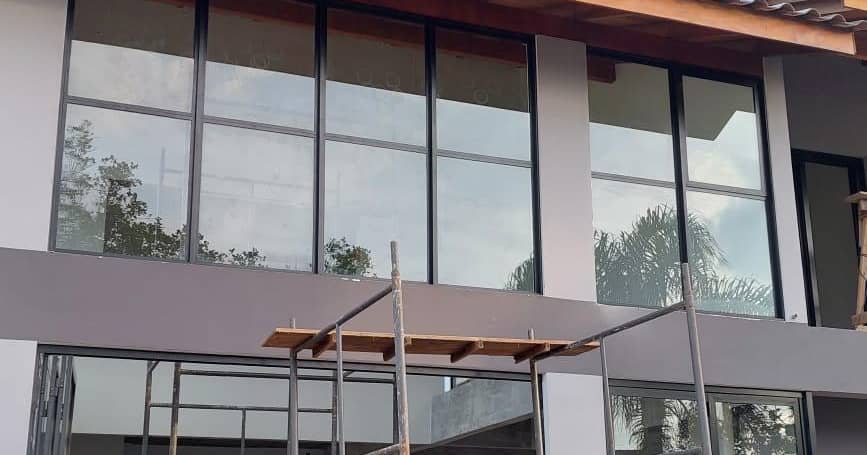 Fachada residencial moderna em construção com grandes esquadrias de vidro e andaime na parte frontal.