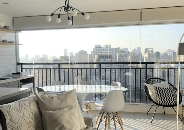 Envidraçamento de Sacada: Como Funciona o Sistema Cortina de Vidro Sala de estar integrada com a varanda através de um sistema de envidraçamento retrátil (cortina de vidro), com vista para a cidade de um andar alto