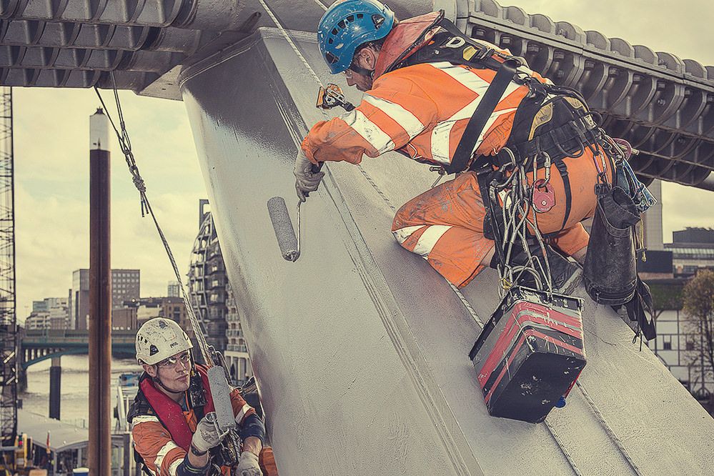 Equipe de alpinismo industrial da Networking Engenharia, com equipamentos de segurança, realizando a pintura e manutenção de uma grande estrutura metálica.