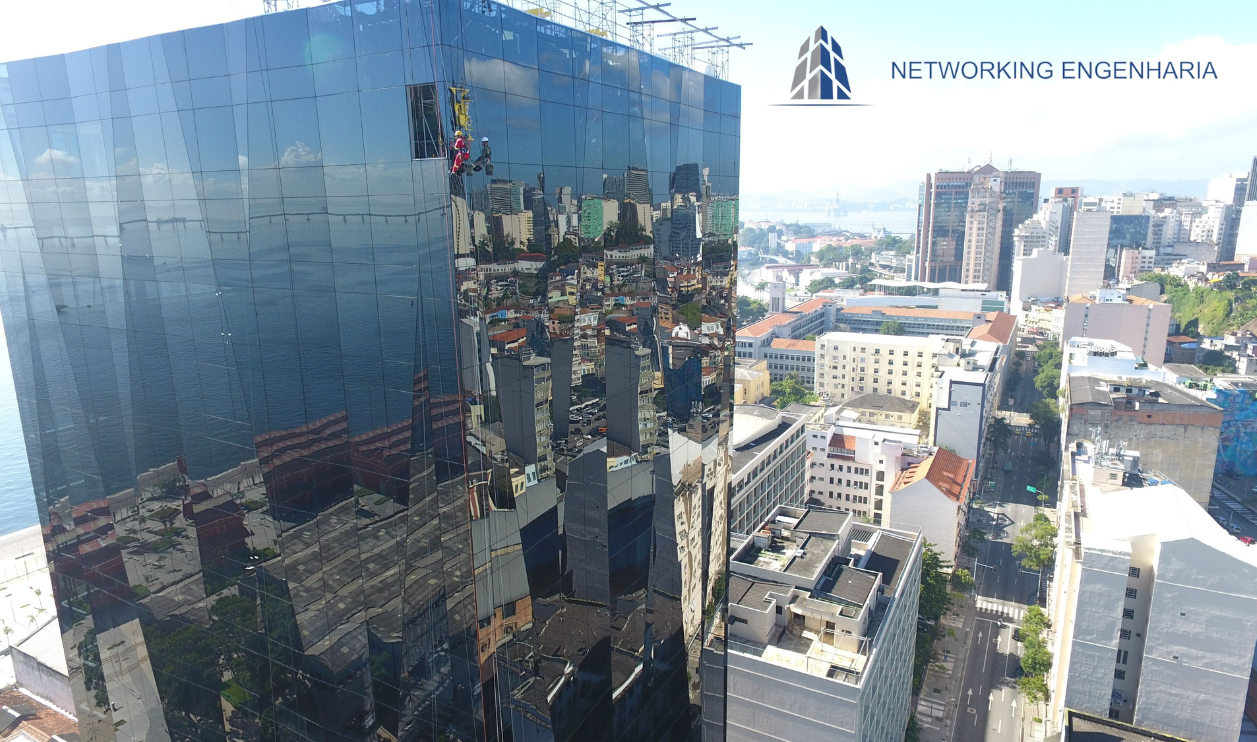 Networking Engenharia: Soluções de Alpinismo Industrial para os Maiores Prédios do RJ Vista aérea de um técnico da Networking Engenharia realizando manutenção com alpinismo industrial na fachada espelhada de um arranha-céu no Rio de Janeiro.