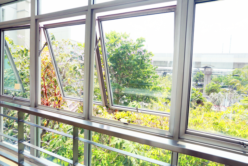 Ampla janela com esquadrias de alumínio em cor natural, composta por painéis fixos e janelas do tipo maxim-ar abertas, com vista para uma área arborizada.