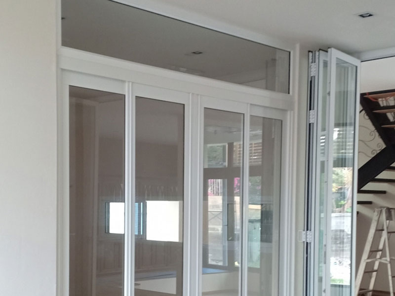 Solução de esquadrias de alumínio branco para um vão grande, combinando uma porta de correr de múltiplas folhas com uma porta articulada (camarão) e uma bandeira de vidro fixa na parte superior.