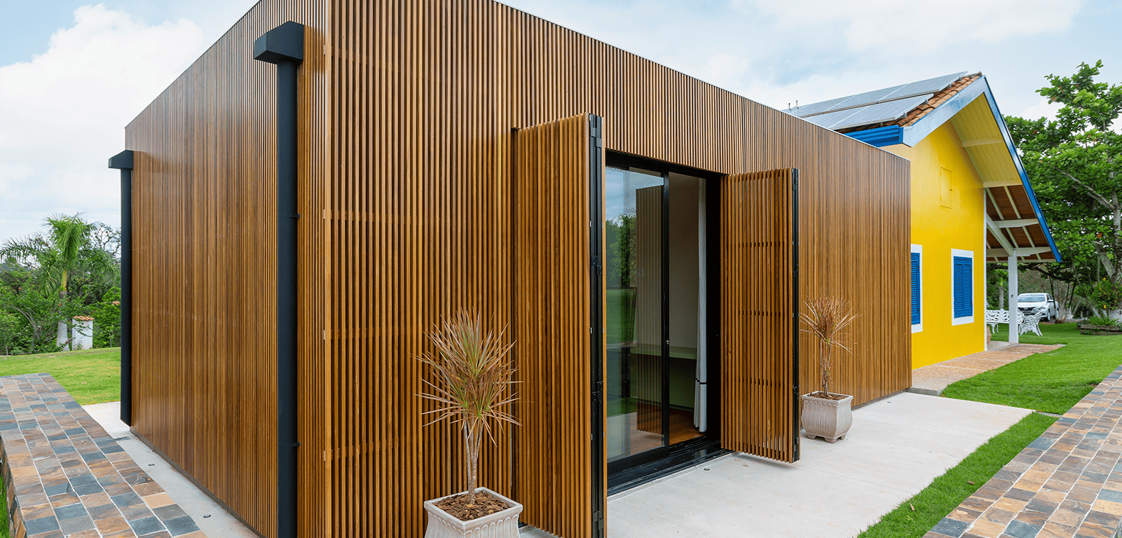 Fachada de um anexo moderno todo revestido com painel de madeira ripada, com uma porta de vidro de correr embutida nas ripas de madeira.