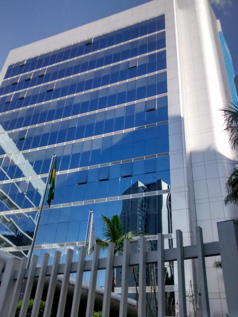 Fachada de um prédio comercial moderno com sistema pele de vidro azul refletivo, janelas maxim-ar abertas e painéis de ACM branco nas laterais.