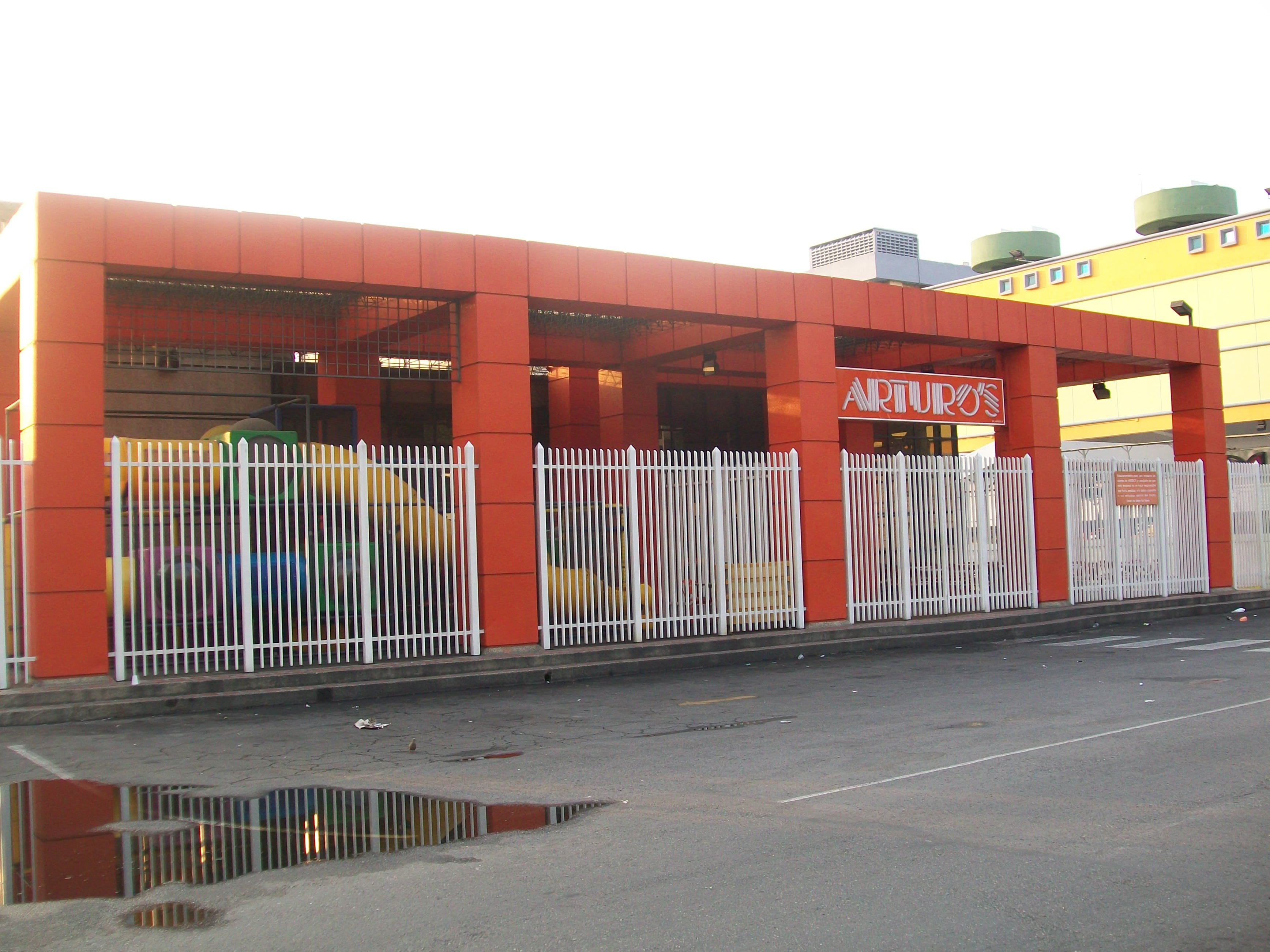 Exemplo de fachada com revestimento em ACM para criar uma identidade visual marcante em um ponto comercial, com estrutura na cor laranja e cercas brancas. Fachada do estabelecimento comercial Arturo's, com uma grande estrutura externa revestida em painéis de ACM na cor laranja.