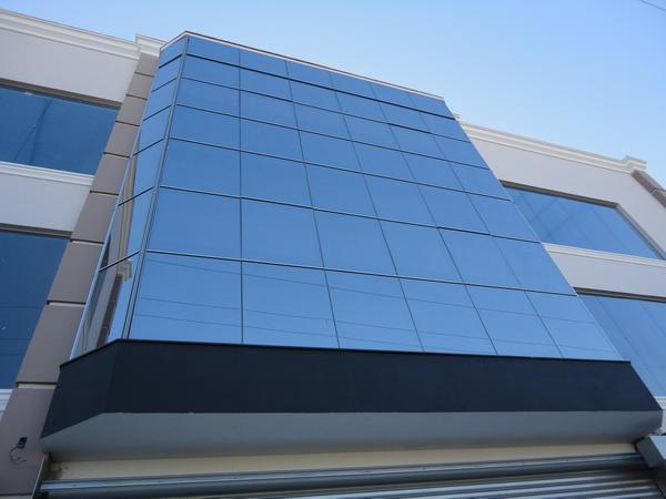 Detalhe da fachada de um prédio comercial com revestimento em pele de vidro refletivo azulado, criando um visual moderno e espelhado.