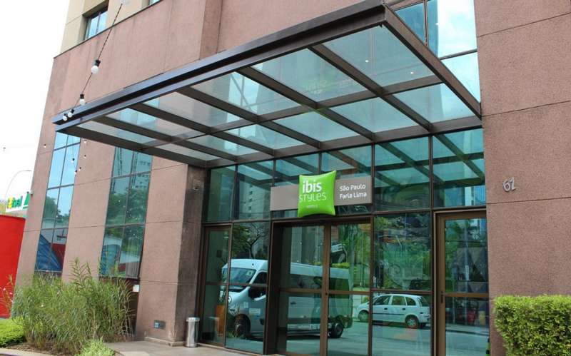 Marquises e Telhados de Vidro para Entradas Comerciais e Prediais Entrada do hotel Ibis Styles com uma marquise de vidro suspensa sobre estrutura metálica marrom, protegendo a porta automática e integrada à fachada de vidro