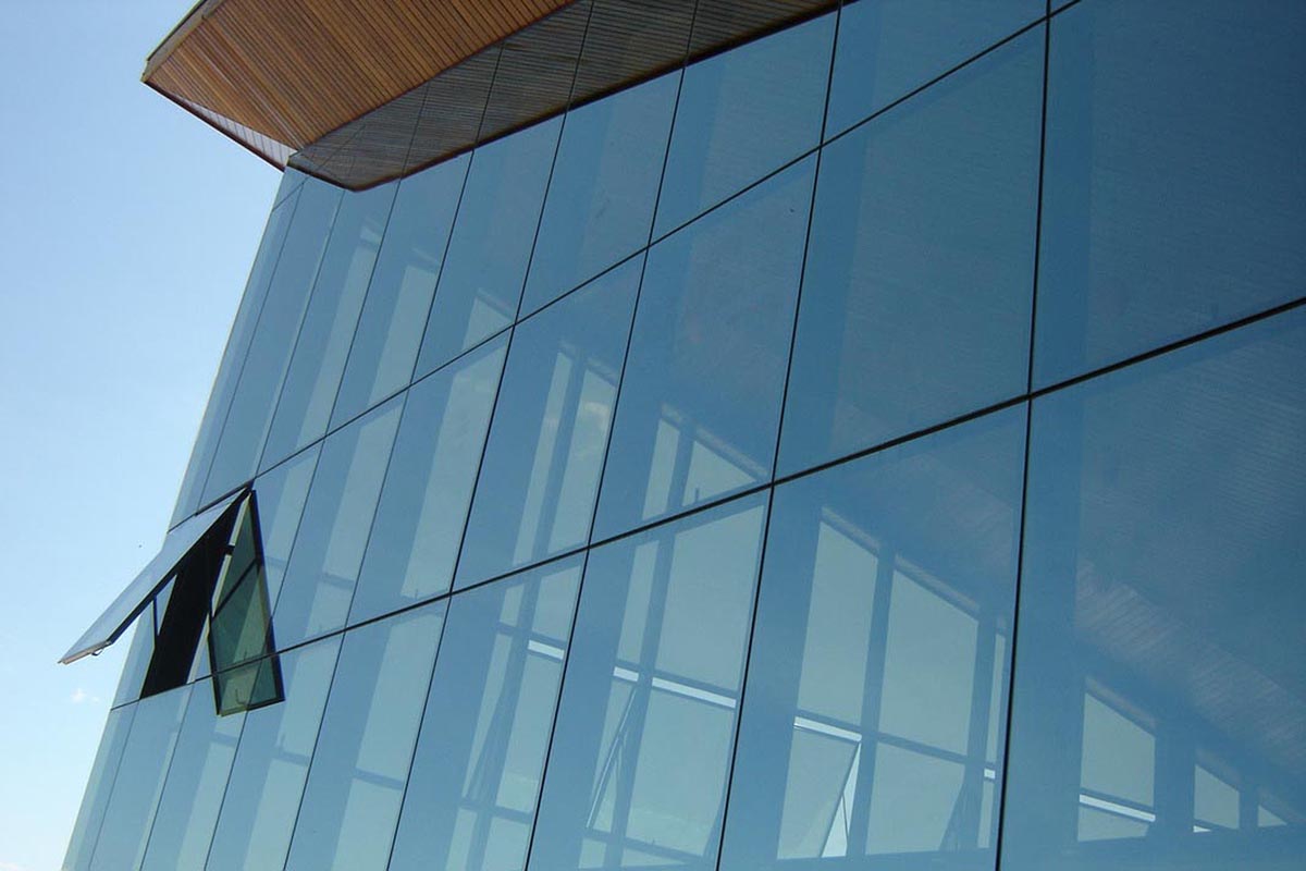 Fachada de edifício moderno com pele de vidro azul refletivo e janelas basculantes abertas.