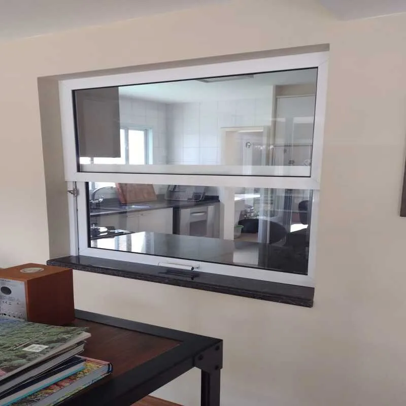 Janela de Correr Vertical (Guilhotina) em Alumínio Branco Janela de correr vertical (guilhotina) com esquadria de alumínio branco, aberta na parte inferior, instalada em uma parede bege com vista para uma cozinha clara.