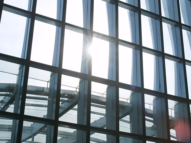 Fachada de vidro recebendo luz solar direta, ilustrando a importância do vidro de proteção solar (controle solar) para reduzir o calor e o brilho excessivo em comparação ao vidro comum.