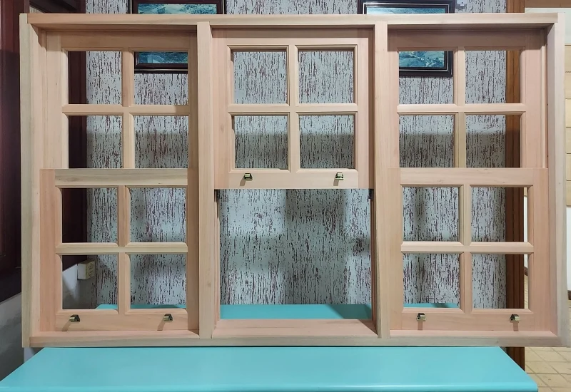 Janelas de Madeira e Alumínio em Mesquita (RJ) | Fale com a Networking Engenharia Conjunto de janelas de madeira em tom claro, com uma janela guilhotina central e painéis laterais, todos com vidros quadriculados em estilo colonial.