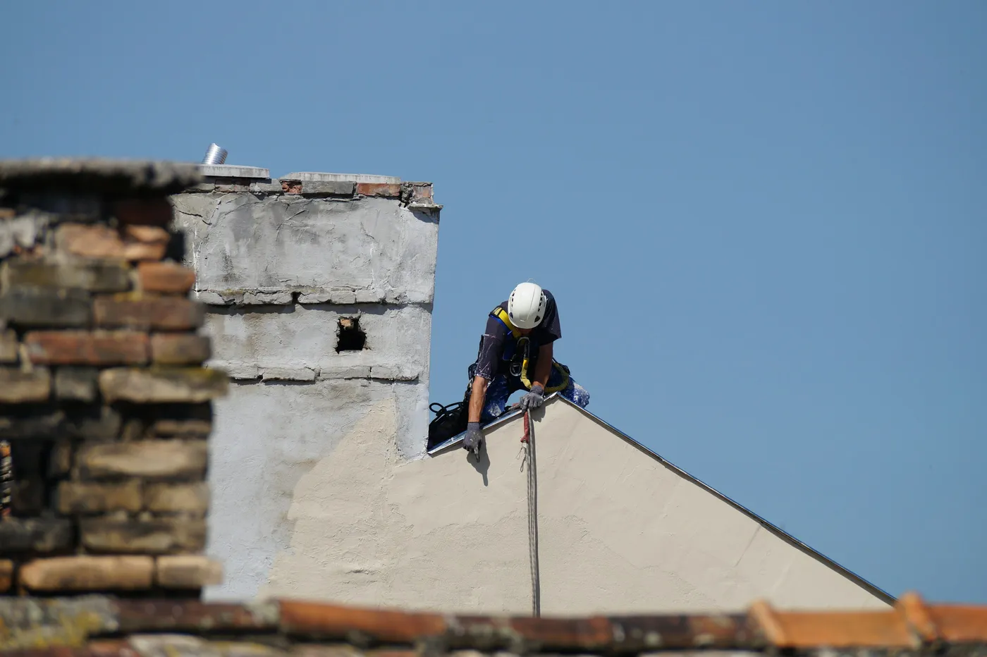 Profissional de acesso por corda realizando trabalho em altura na cobertura de um prédio, com capacete e linha de vida