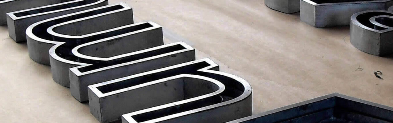 Processo de fabricação de letreiro, mostrando várias letras caixa de metal sendo preparadas em uma oficina para compor a comunicação visual de uma fachada.