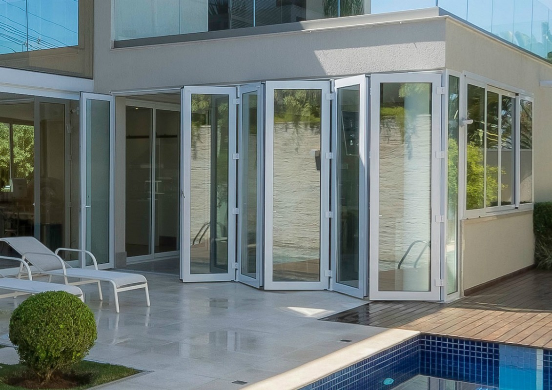 Exemplo de material para esquadria: uma porta de vidro articulada (camarão) fabricada em alumínio branco, integrando a casa com a área da piscina.