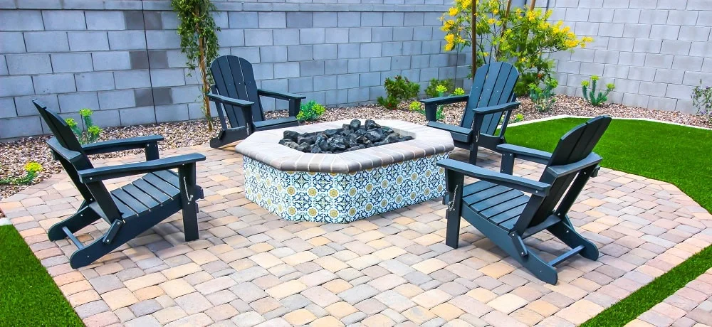 Área de lazer com uma lareira externa (fire pit) revestida de azulejos decorativos, piso de bloquetes e um muro de blocos de concreto ao fundo.