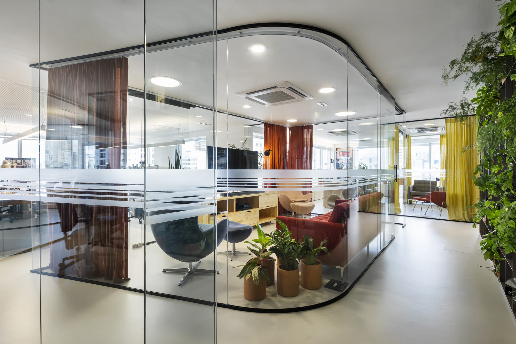 Escritório moderno com uma sala de reunião criada por uma parede de vidro curva com faixas jateadas para privacidade, otimizando o espaço de forma elegante