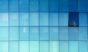 Manutenção e Troca de Vidros em Fachadas Glazing no RJ Detalhe de fachada em pele de vidro azul com uma janela maxim-ar aberta, demonstrando o sistema de ventilação integrado à estrutura glazing.