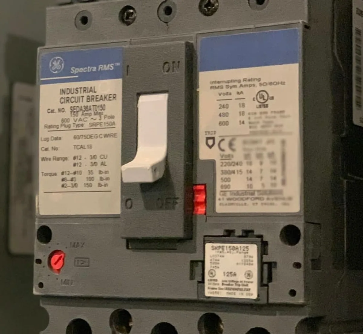 Detalhe da etiqueta técnica e da chave liga-desliga de um disjuntor industrial em quadro elétrico