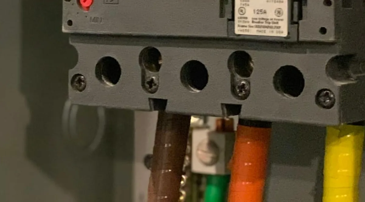 Terminais e fiação colorida conectados na base de um disjuntor industrial em quadro elétrico