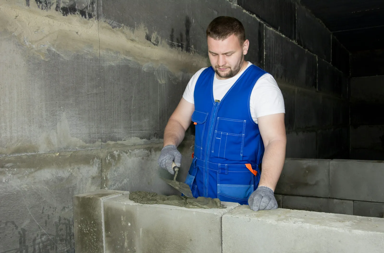 Recuperação estrutural de concreto: aplicação de argamassa de reparo Trabalhador aplicando argamassa de reparo em pilar de concreto durante obra de recuperação estrutural