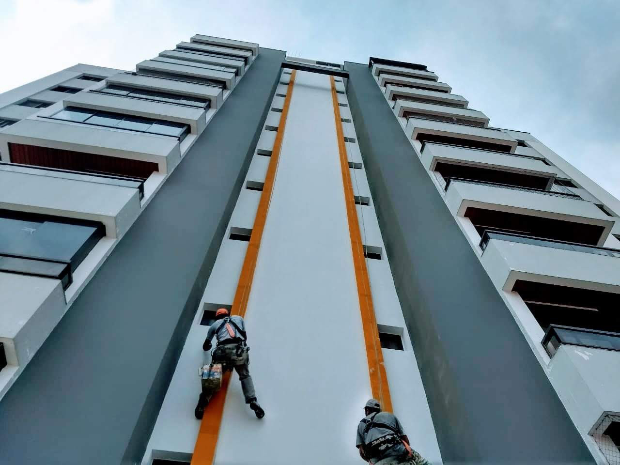 Reforma e Manutenção de Fachadas Prediais com Alpinismo Industrial Equipe de alpinismo industrial da Networking Engenharia realizando a reforma e pintura da fachada de um prédio residencial alto, utilizando técnicas de rapel e equipamentos de segurança.