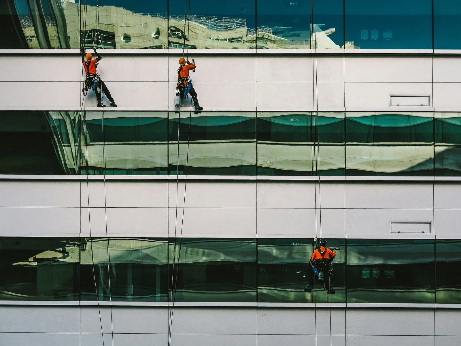 Técnicos de acesso por corda inspecionam a fachada de vidro de um edifício durante um serviço de manutenção predial