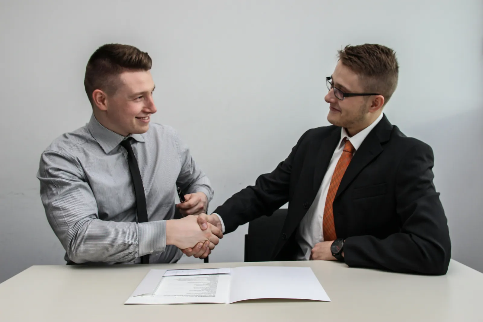 Dois profissionais selando com aperto de mãos a assinatura de um contrato de manutenção predial sobre a mesa