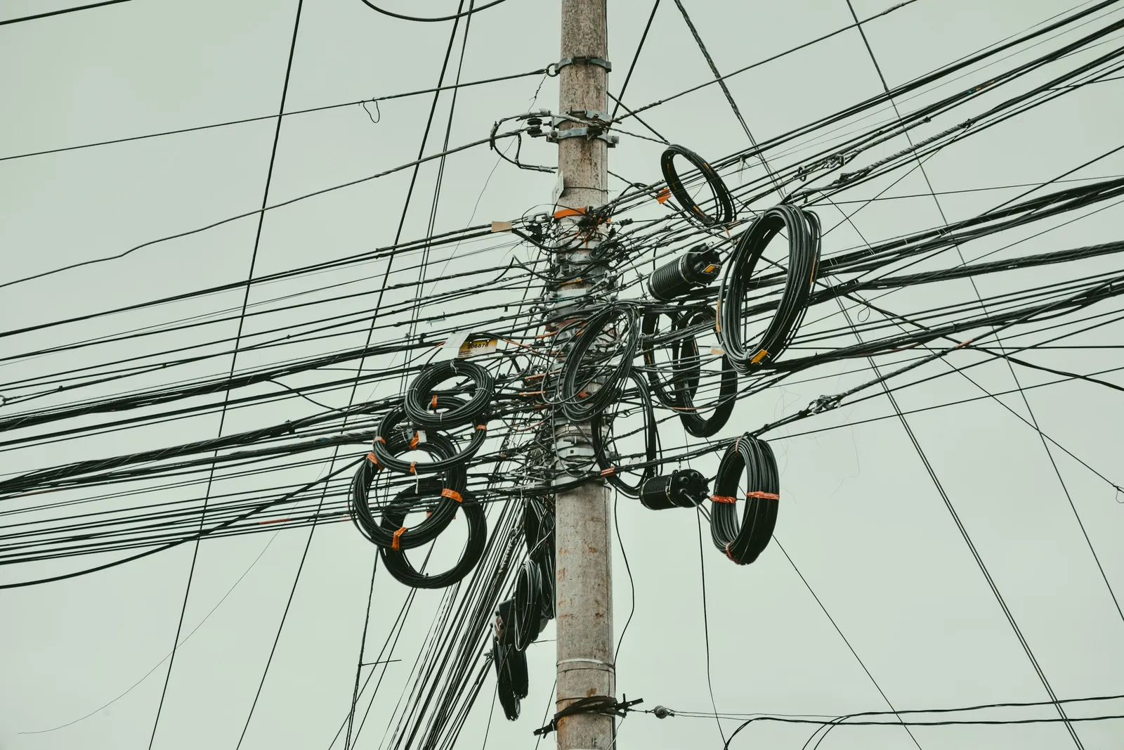 Fios e cabos elétricos emaranhados em poste de rede, ilustrando o risco de sobrecarga elétrica sem manutenção