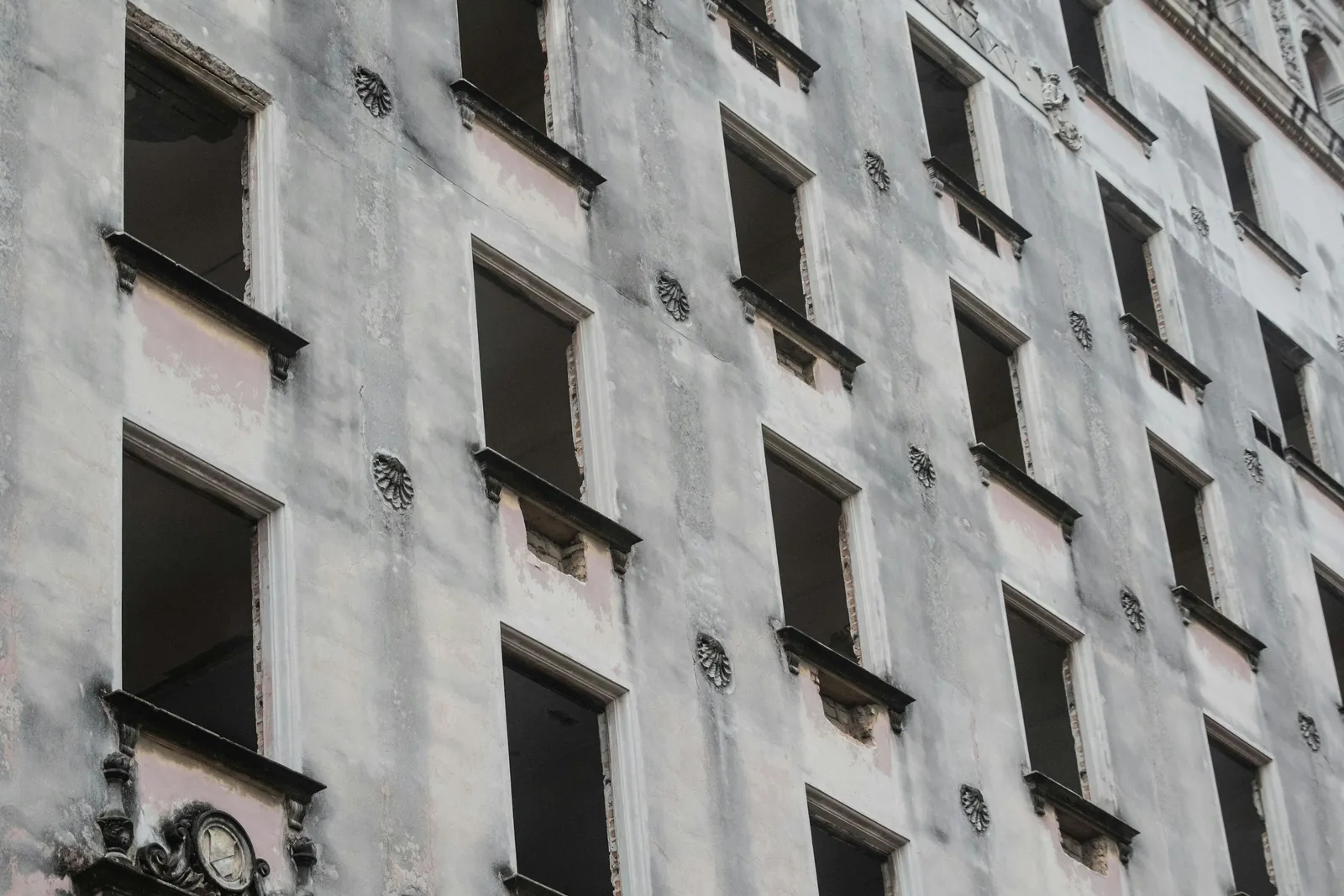 Fachada de prédio antigo com janelas danificadas e reboco descascando, sinal de manutenção predial negligenciada