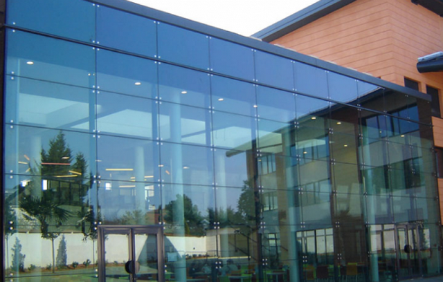 Fachada em pele de vidro com Sistema Spider, mostrando os painéis de vidro fixados por garras de metal (aranhas) que garantem máxima transparência e um visual clean.