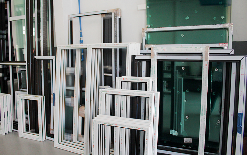 Showroom ou fábrica com diversos tipos de esquadrias de alumínio, incluindo janelas e portas de correr e de abrir, nas cores branca e preta.
