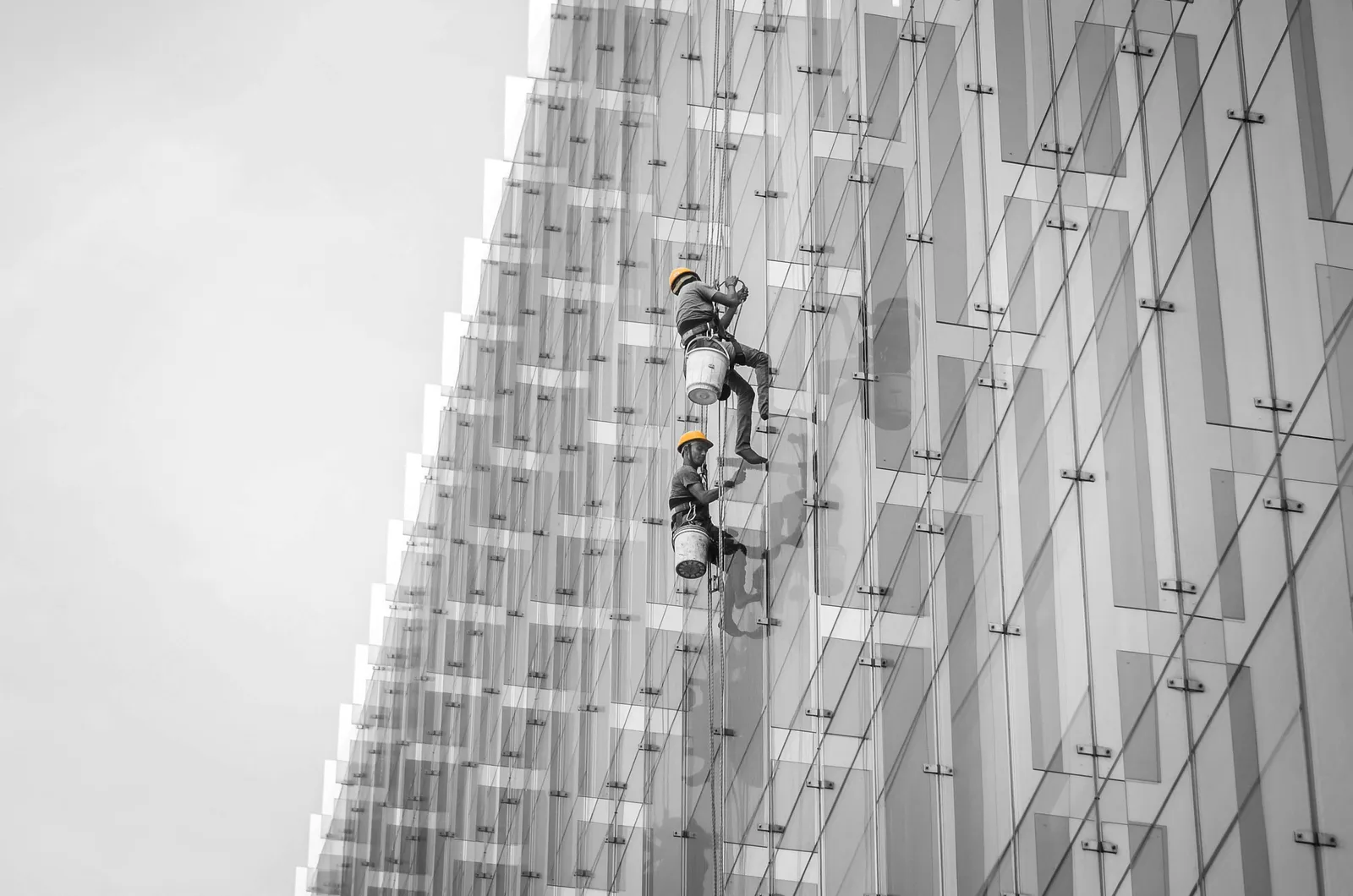 Profissionais de alpinismo industrial em rapel executando servico em fachada de vidro, conforme a NR-35