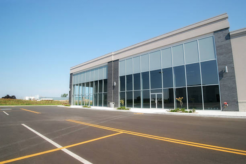 Fachada comercial moderna com amplas janelas de vidro espelhado e estacionamento vazio em frente.
