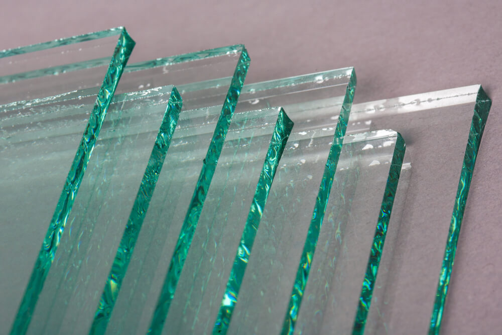 Chapas de vidro comum (float) empilhadas, destacando a intensa cor esverdeada característica de suas bordas e sua estrutura simples