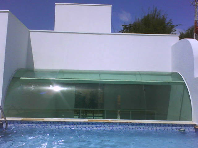Estrutura de cobertura em vidro curvo translúcido instalada sobre área de piscina residencial, destacando design moderno e aproveitamento de luz natural.