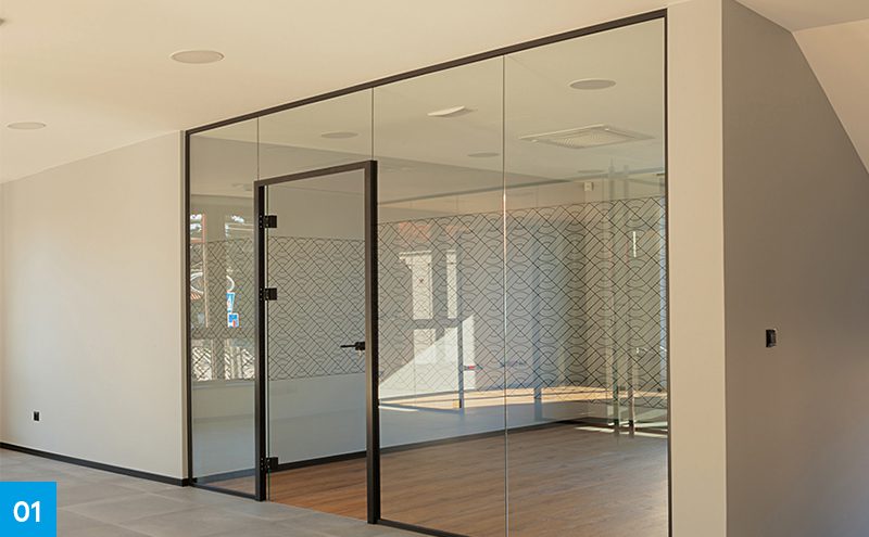 Divisória de vidro do chão ao teto com esquadria fina de alumínio preto e porta de abrir, separando uma sala de reuniões em um escritório moderno.