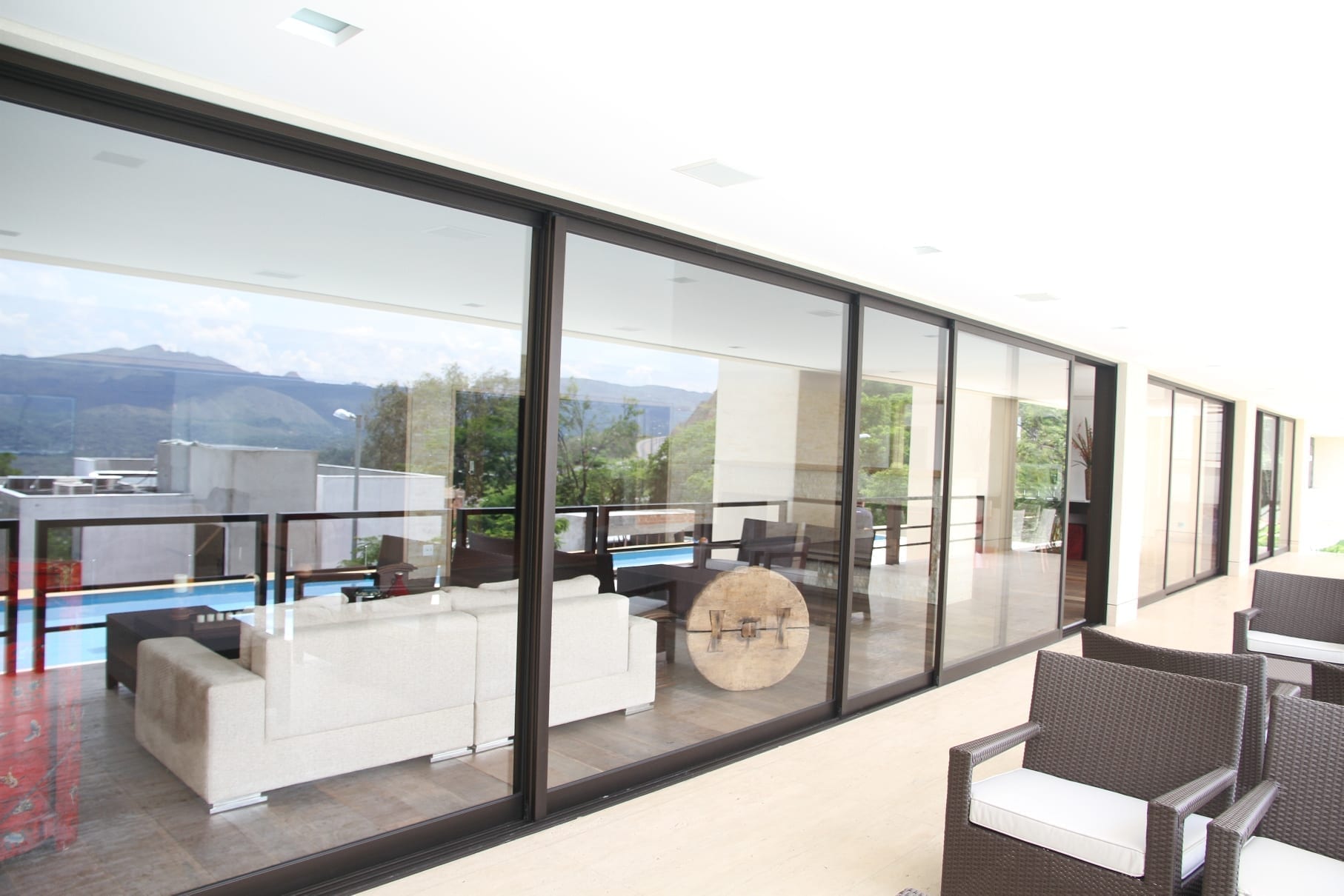 Fachada de casa de alto padrão com grandes portas de correr de vidro e esquadrias pretas, integrando a sala de estar com a varanda externa e a piscina.