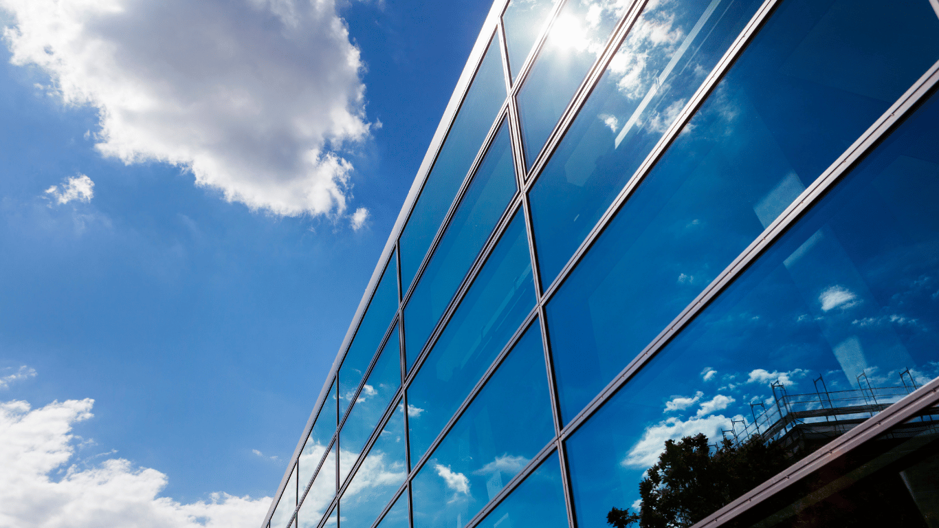 Fachada moderna com ampla cobertura de vidro refletindo o céu.