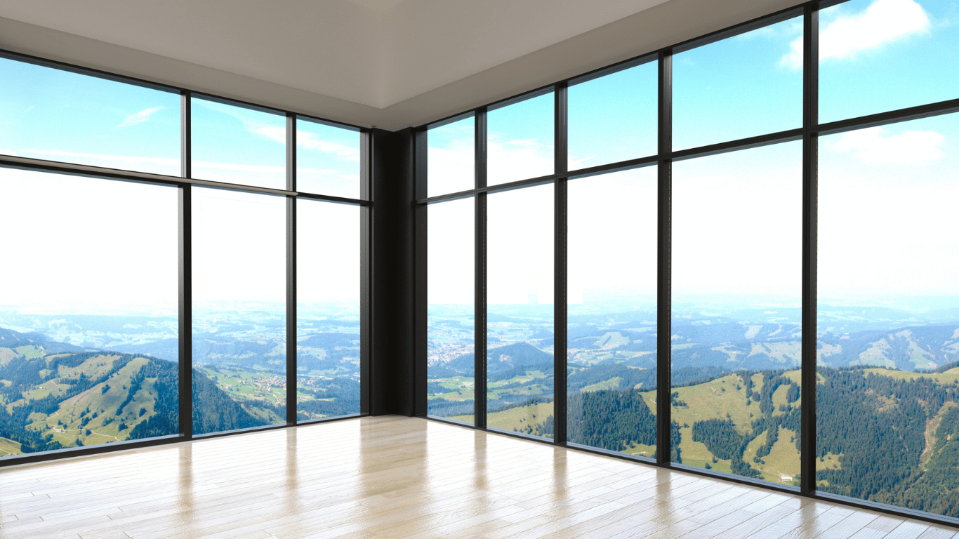 Sala com muro de vidro proporcionando ampla vista para o campo e montanhas ao fundo.