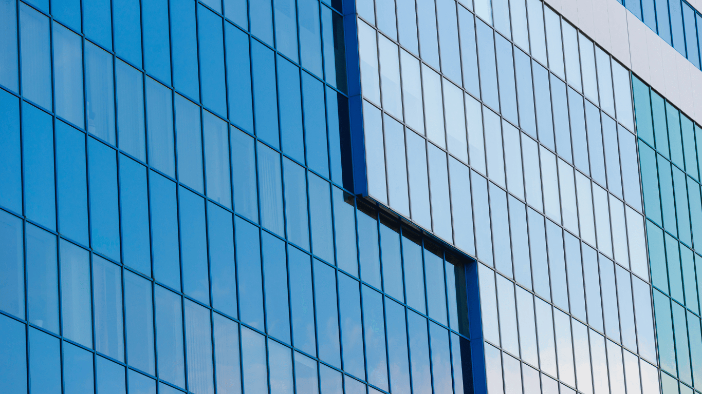 Como manter a limpeza de fachadas em pele de vidro, Fachada em pele de vidro azul refletindo o céu em edifício comercial moderno.