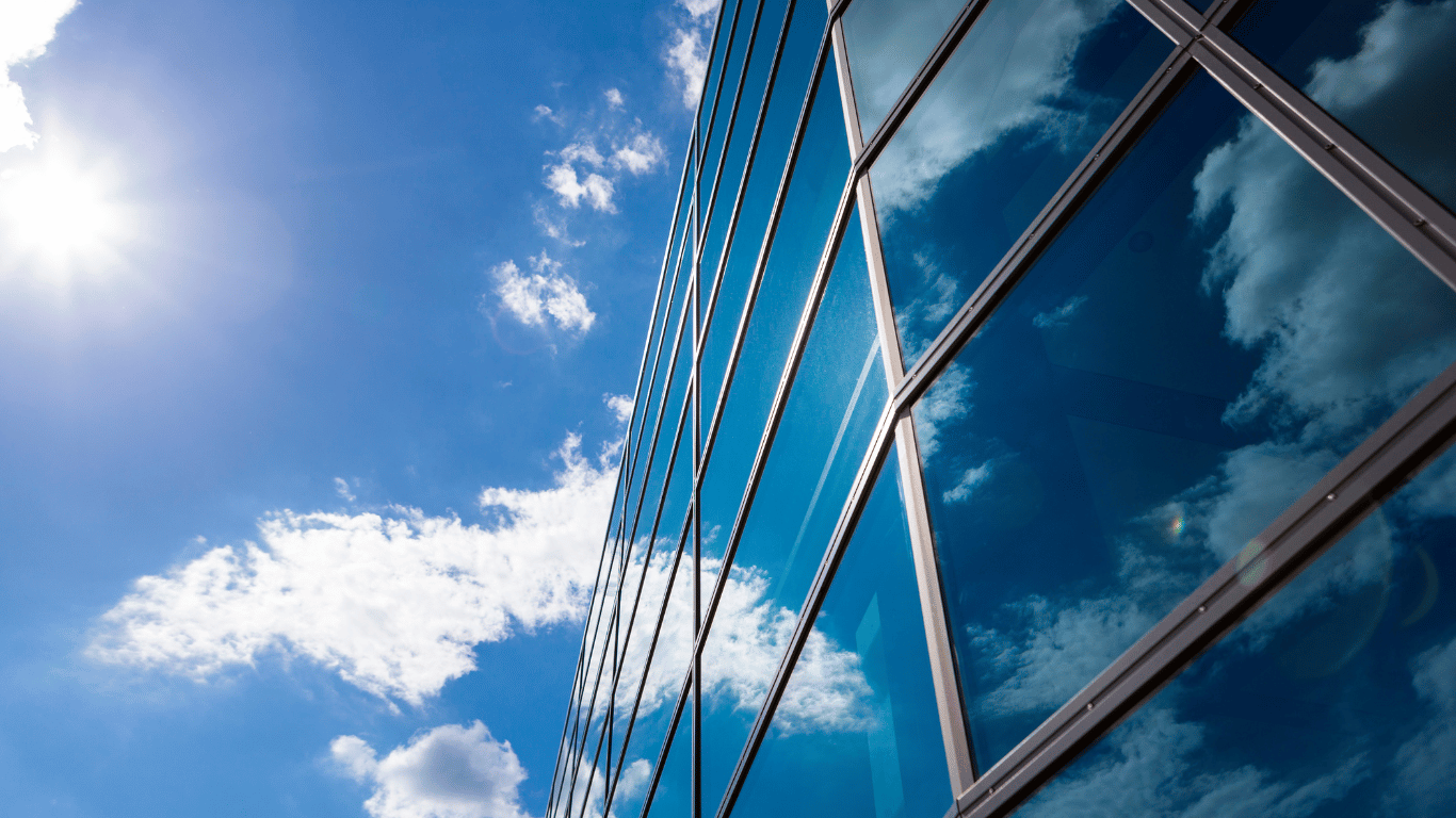 Fachada de vidro refletindo o céu com pé direito duplo em edifício moderno.