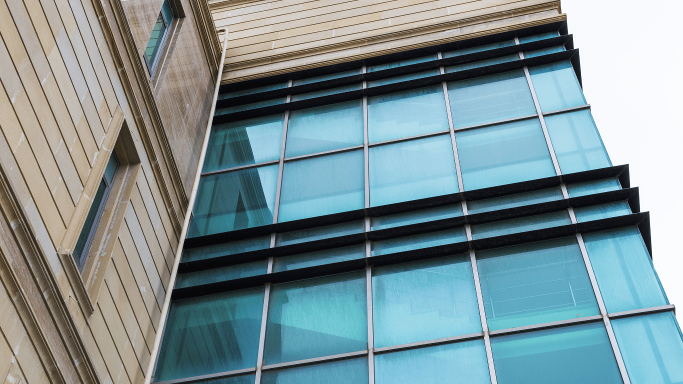 Fachada de edifício moderno com sistema spider glass, destacando a estrutura de vidro e suportes metálicos.